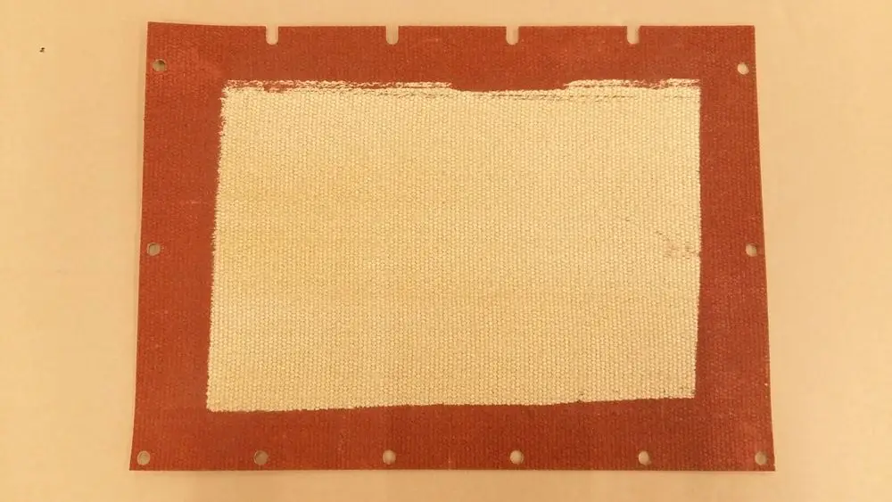 Isolierdeckel aus rotem Material mit einem weißen, strukturierten Bereich in der Mitte, befestigt mit Ösen. Produkt von Remeha.